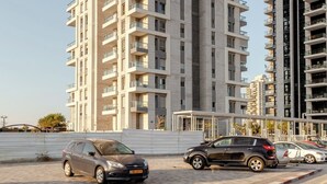 Un edificio de gran altura con varios balcones y un estacionamiento con coches.