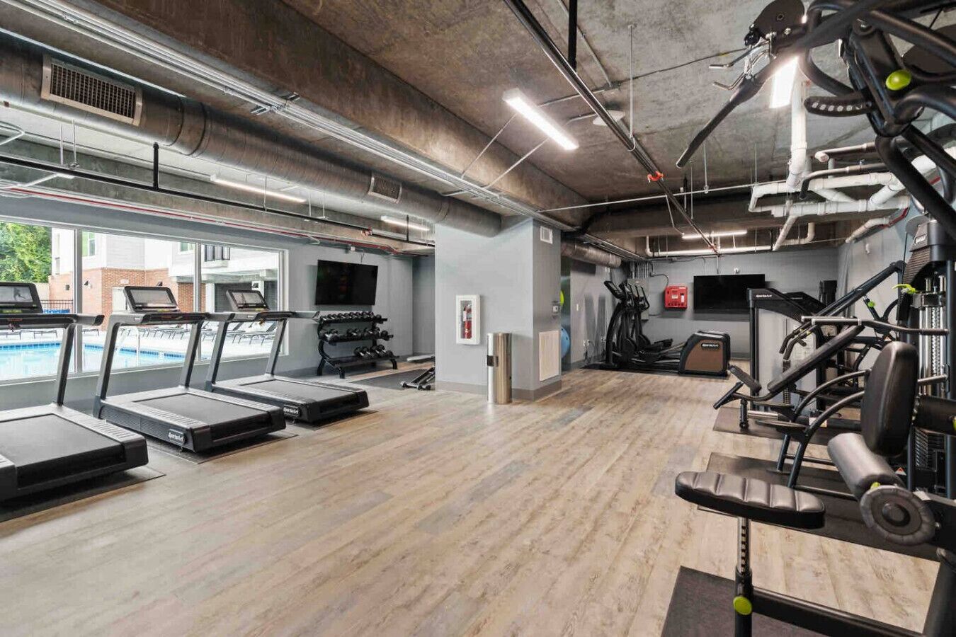 A gym with treadmills, weight machines, and a pool area visible through the windows.