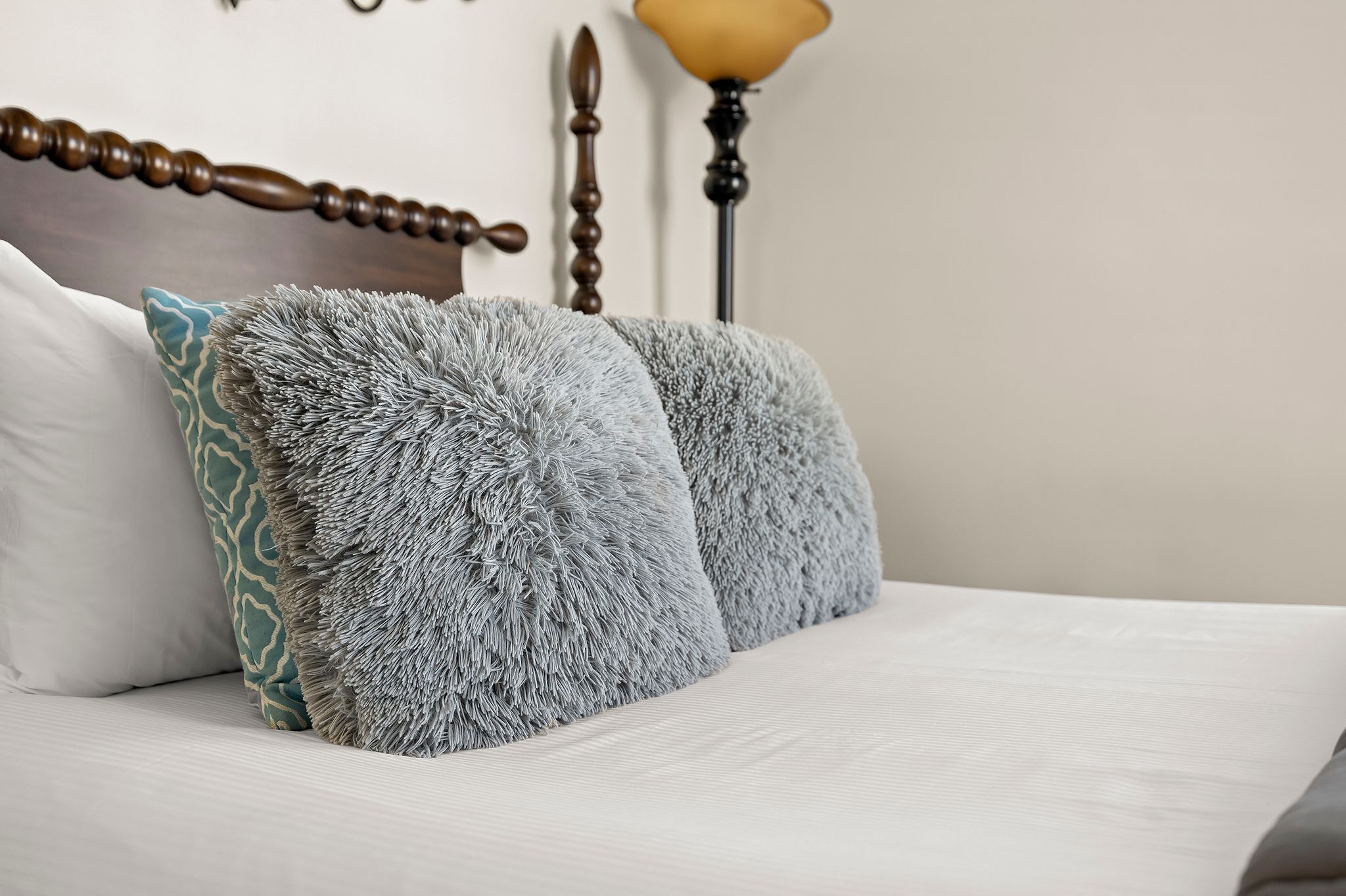 A bed with a wooden headboard, two fluffy grey pillows, and a patterned pillow.