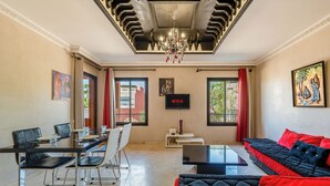 A modern hotel room with a dining area, a sofa, a TV, and a chandelier.