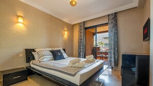 A modern hotel room with a large bed, two wall sconces, a flat-screen TV, and a view of the outdoor balcony.