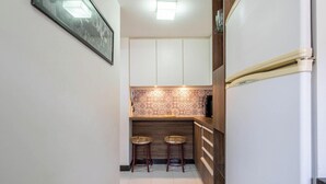 A narrow kitchen with white cabinets, a patterned backsplash, and two wicker stools.