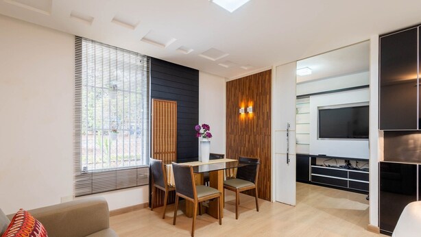 A modern kitchen with a built-in oven, a dining area with a table and chairs, and a large window with blinds.