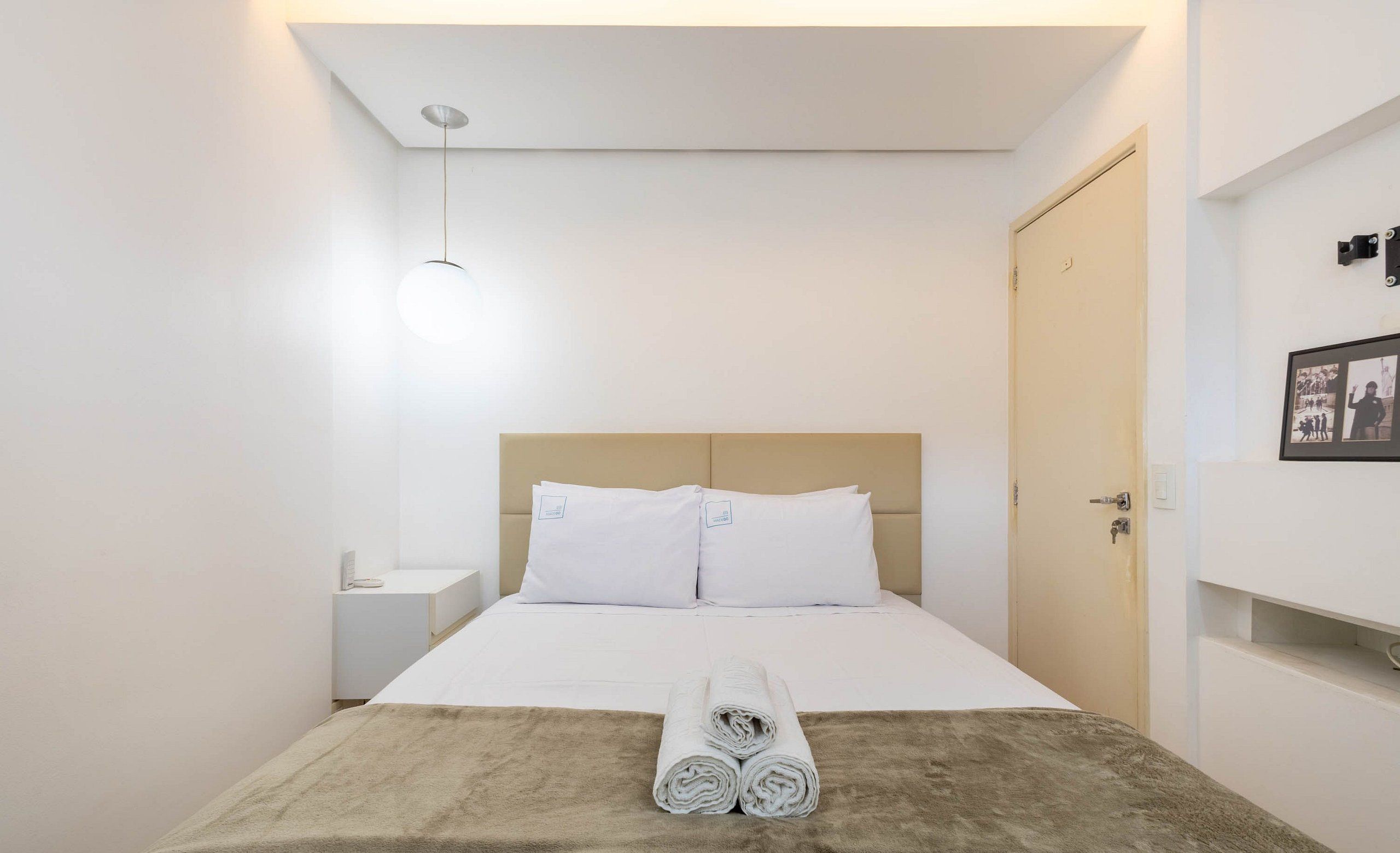 Una cama bien hecha con sábanas blancas, un edredón marrón y toallas enrolladas sobre la cama.