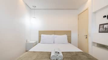 Una cama bien hecha con sábanas blancas, un edredón marrón y toallas enrolladas sobre la cama.