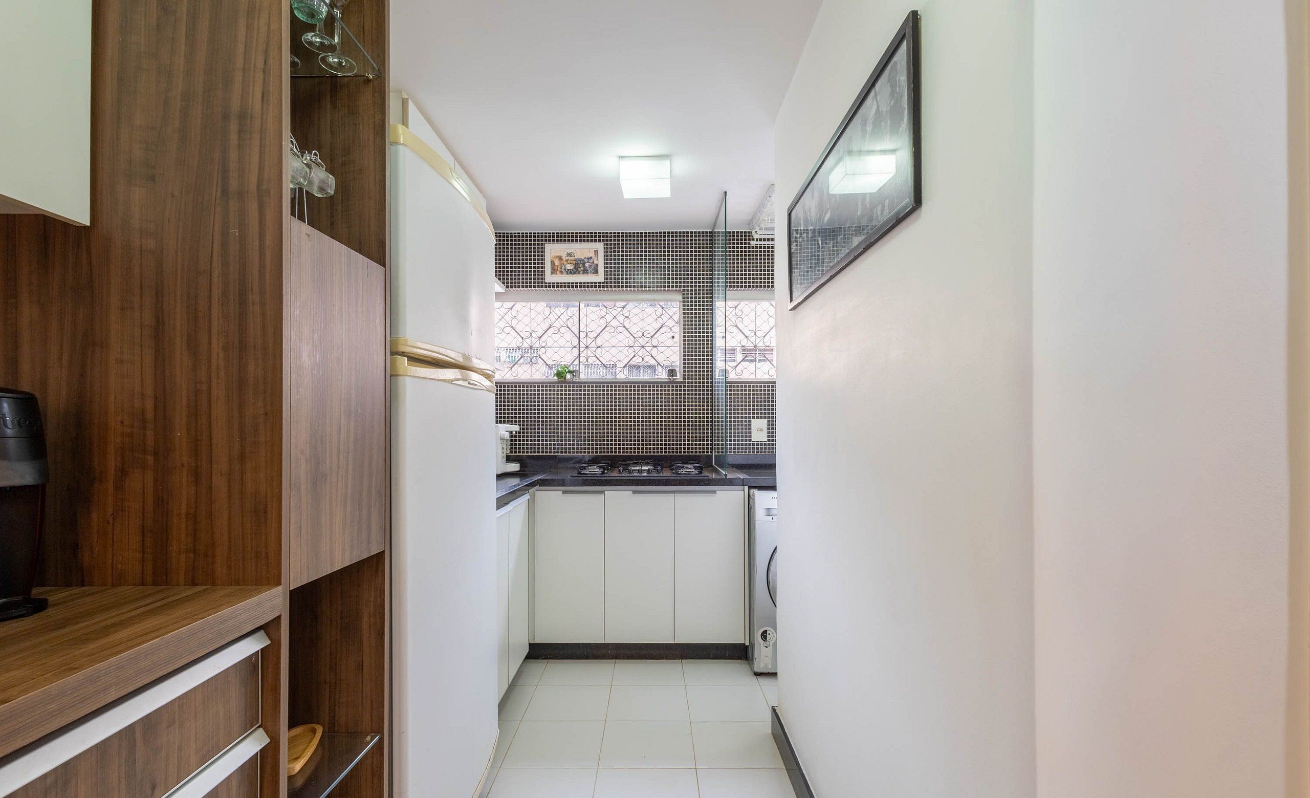 A narrow kitchen with white cabinets, a black countertop, and a tiled backsplash.