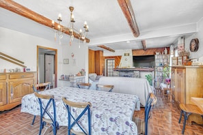 Ein geräumiger Raum mit Esstisch, Stühlen, einer Chandelier, einem Bücherregal und einem Fernseher.