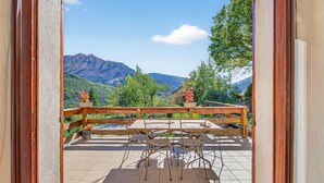 A balcony with a wooden railing, a table, and chairs, overlooking a mountainous landscape.