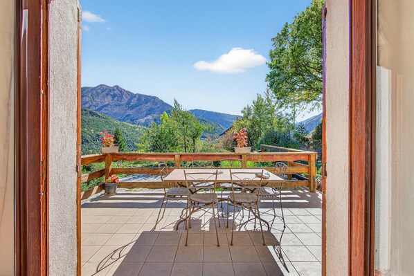 A balcony with a wooden railing, a table, and chairs, overlooking a mountainous landscape.