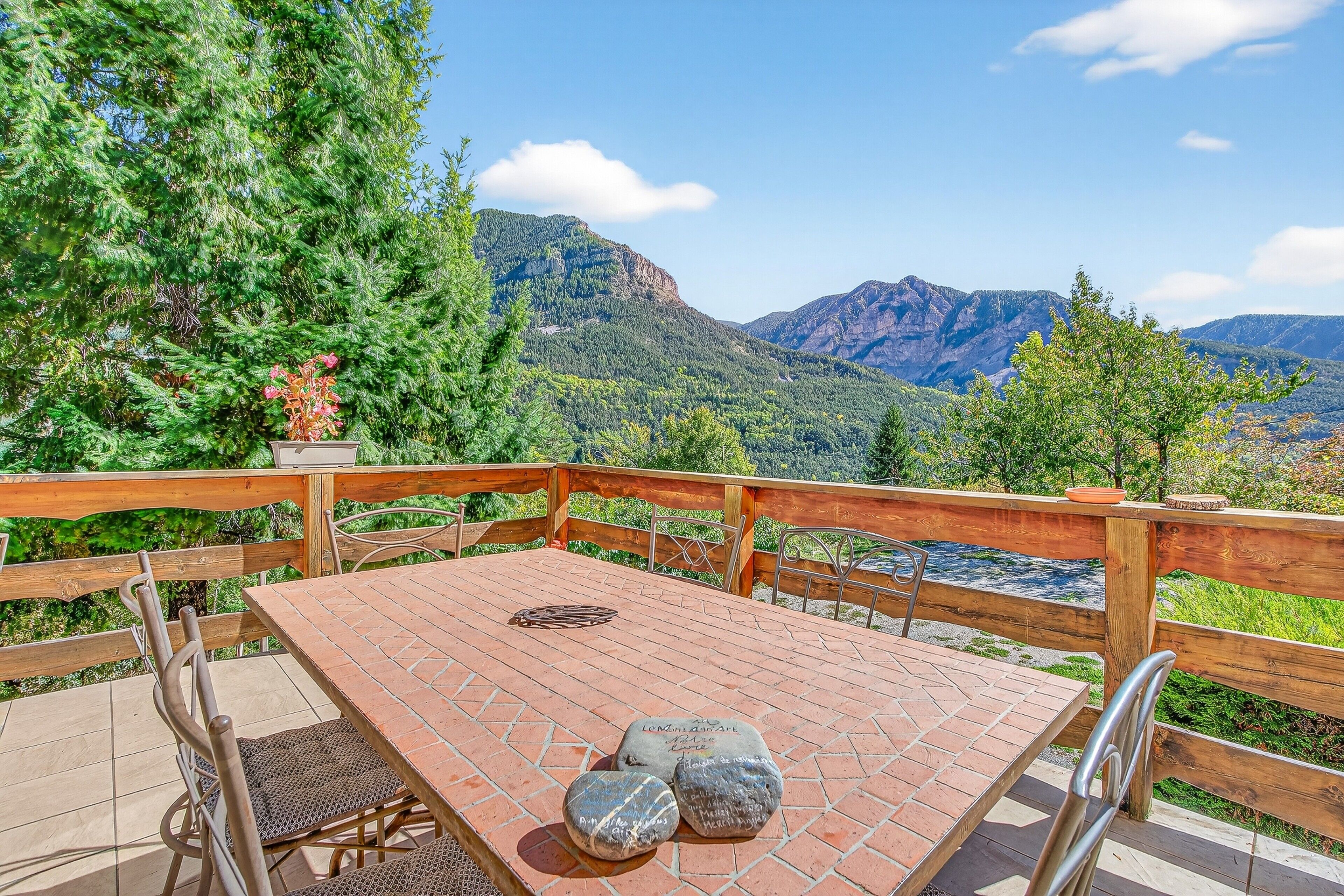 A wooden deck with a table and chairs, overlooking a mountainous landscape.