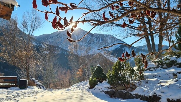 A snow-covered outdoor area with a bench, a wooden structure, and a view of mountains.