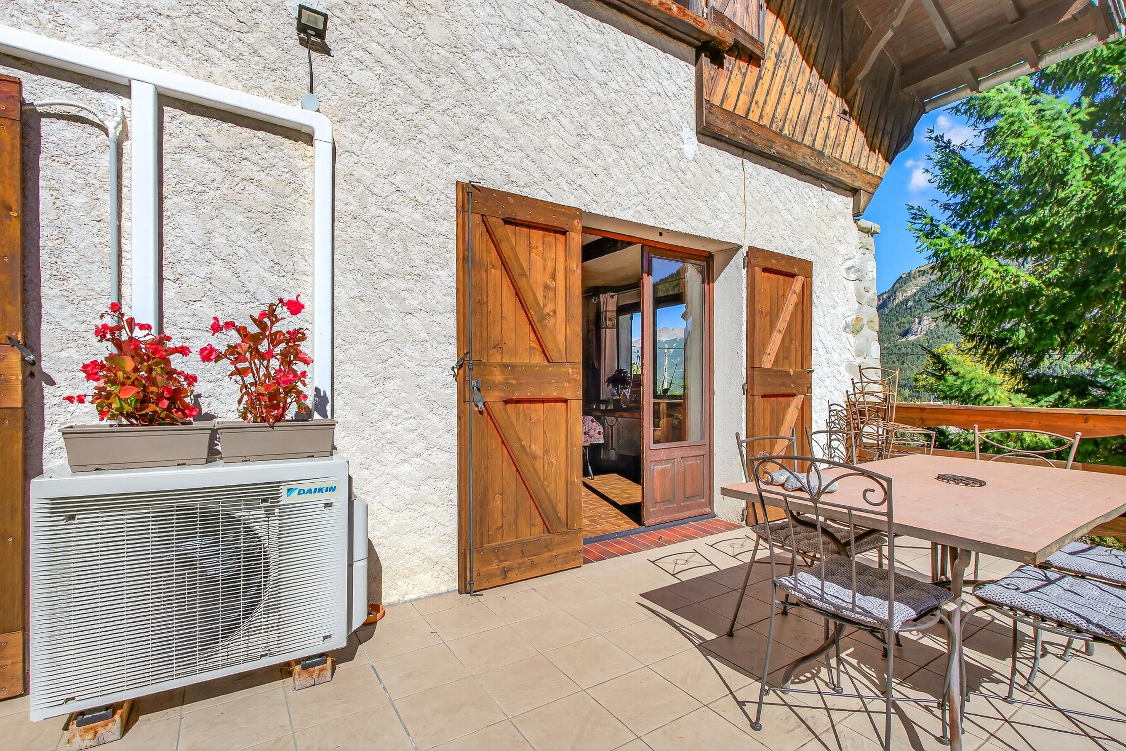 A rustic building with a stone exterior, wooden doors, a table with chairs, and a Daikin air conditioning unit.