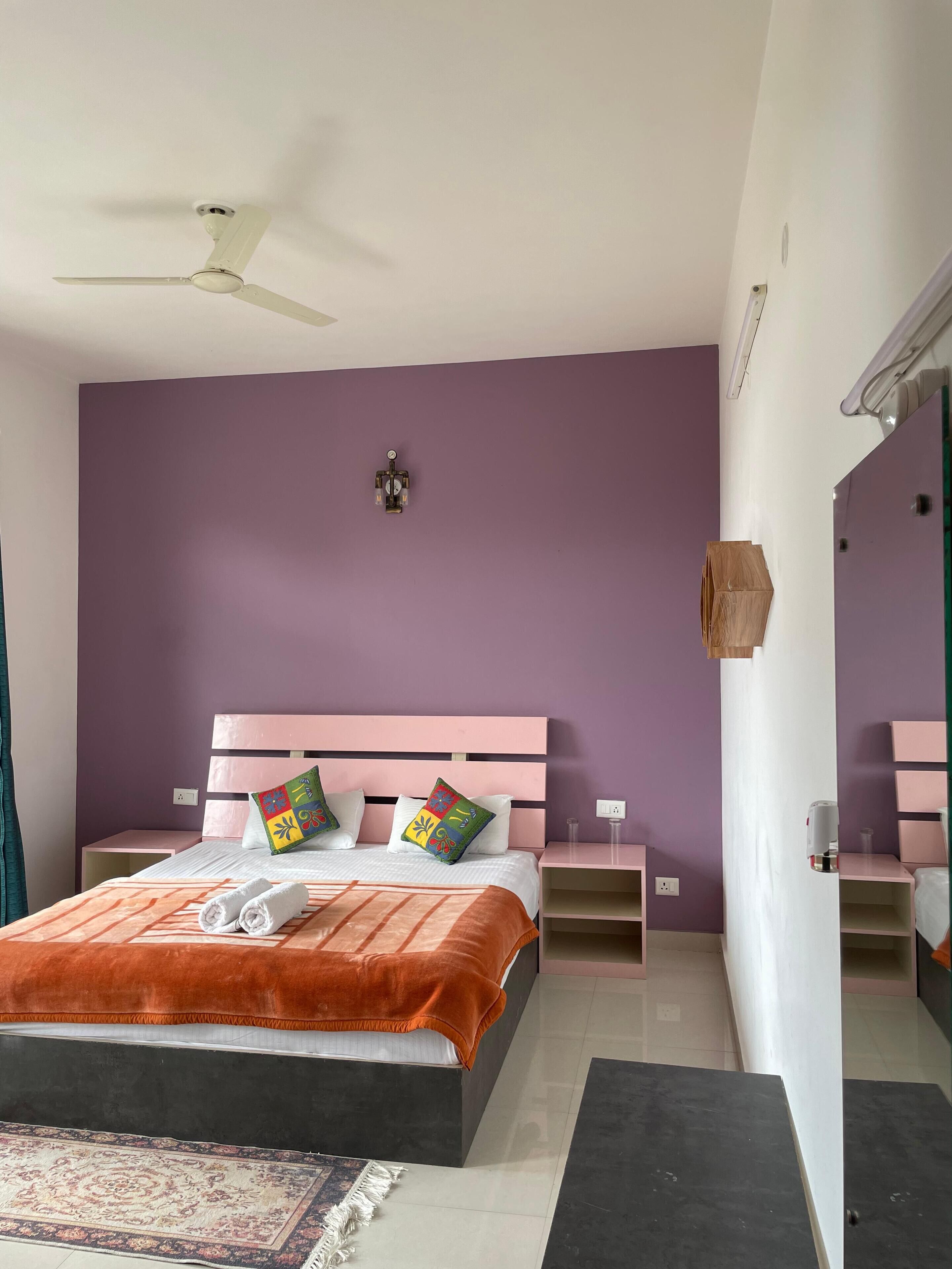 A bedroom with a bed, nightstands, a ceiling fan, a wall-mounted light, and a mirror.