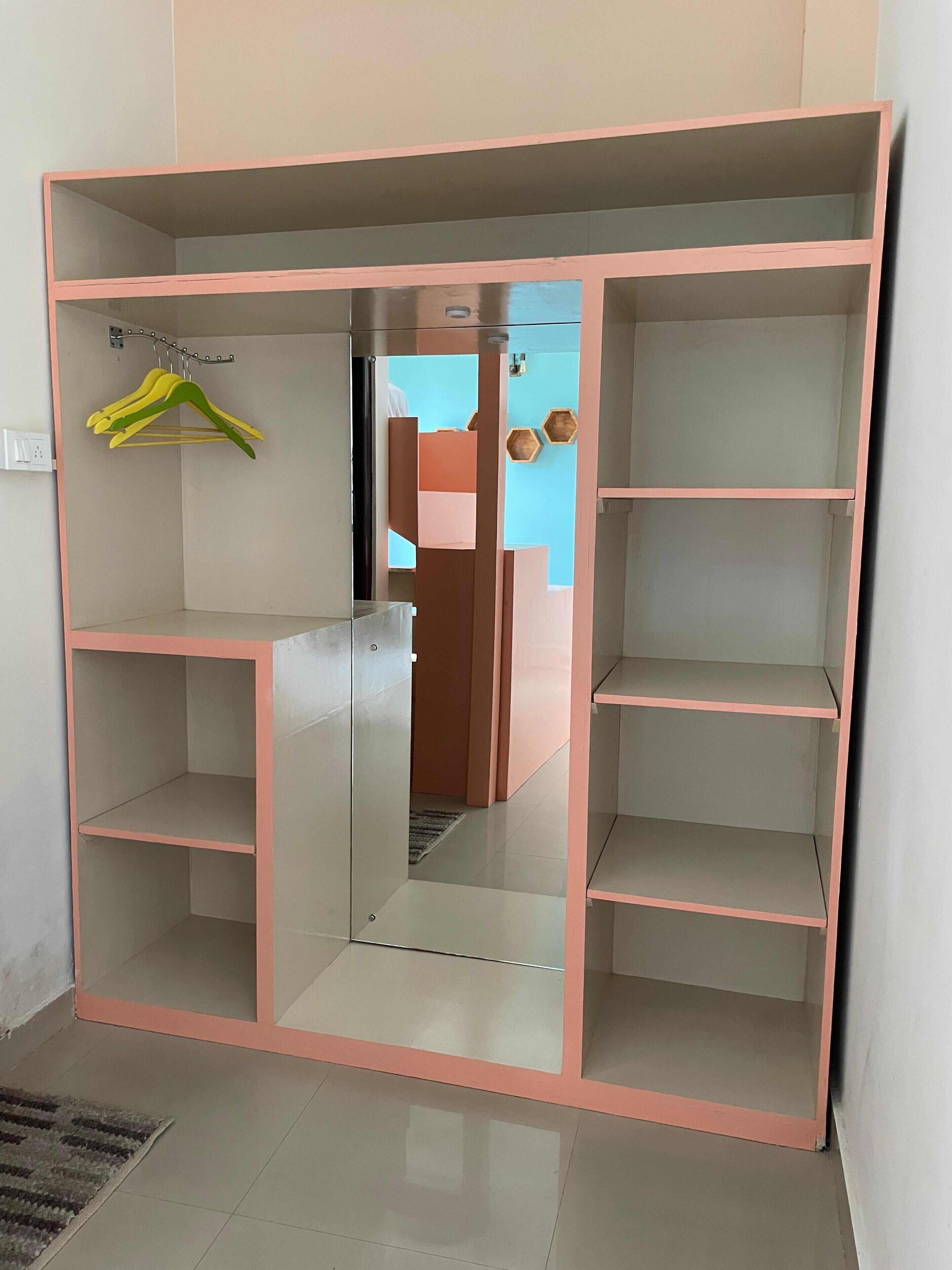 Un armario con varios estantes, espacio para colgar ropa, un espejo y una puerta con pomo.