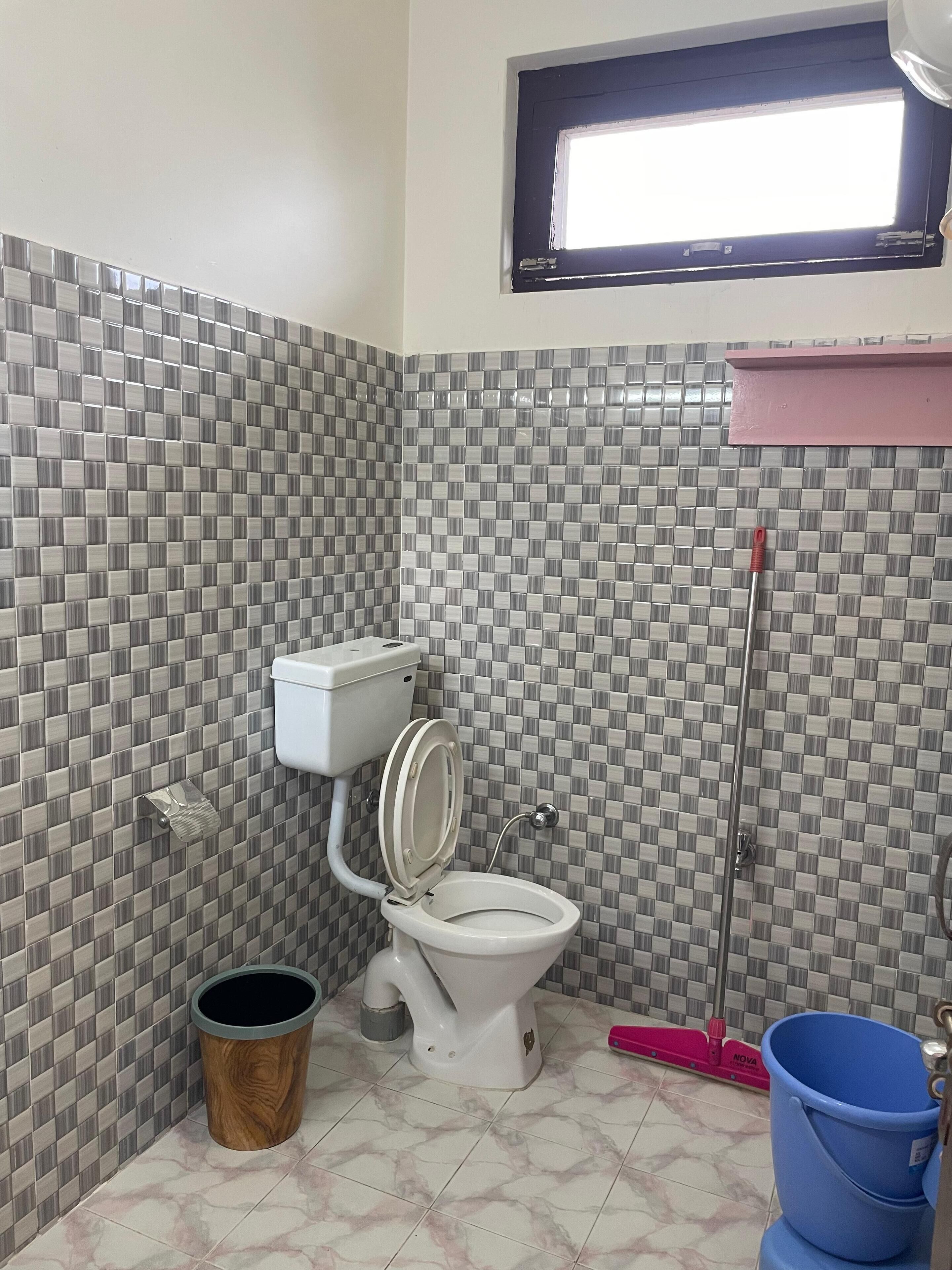 A bathroom with a toilet, a wooden trash bin, a mop, and a bucket.