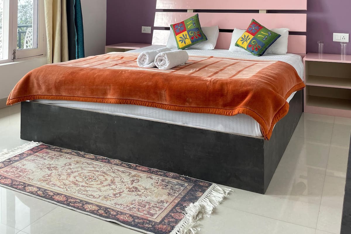 A bedroom with a bed, a nightstand, a window with curtains, and a wall-mounted light fixture.