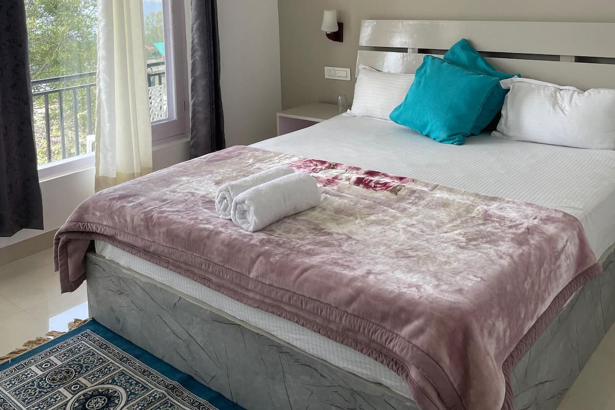 A hotel room with a bed, a ceiling fan, an air conditioning unit, a nightstand, and a window with curtains.