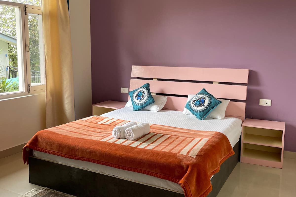 A neatly arranged bedroom with a bed, a bedside table, a nightstand, a patterned rug, and a window with curtains.