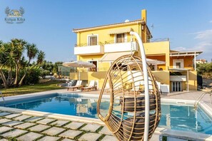 A yellow building with a swimming pool, lounge chairs, and a wicker chair. - Ktima Kika - Private Pool Escape Tranquility (Trifylia)