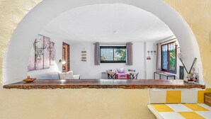 Een kamer met een wit gewelfd plafond, een zithoek met een tafel en stoelen, een raam met gordijnen en uitzicht op de omgeving.