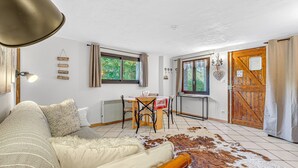 Een gezellige kamer met een bed, een eettafel met stoelen, een houten deur en uitzicht op groen buiten.