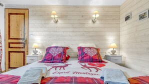 Een slaapkamer met een houten wand, twee nachtkastjes met lampen, een bed met een rood-witte quilt en een deur.