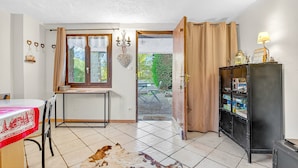 Een kamer met een eettafel, een zwart kastje, een raam met gordijnen en uitzicht op het buiten.
