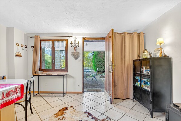 A room with a dining table, a black cabinet, a window with curtains, and a view of the outside.