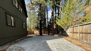 A paved patio area with a wooden fence and tall trees in the background.