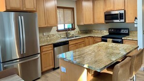 A modern kitchen with wooden cabinets, stainless steel appliances, granite countertops, and a built-in island with bar seating.