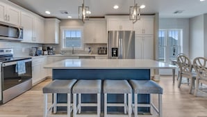 A modern kitchen with white cabinets, stainless steel appliances, and a central island with bar stools. - A Wave From It All.  Great location-short walk to beach and Kure Beach Pier. (Kure Beach)