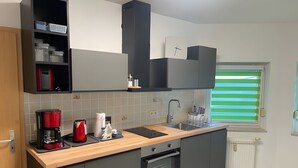 A modern kitchen with grey cabinets, a wooden countertop, a built-in oven, a coffee maker, and a window with blinds.
