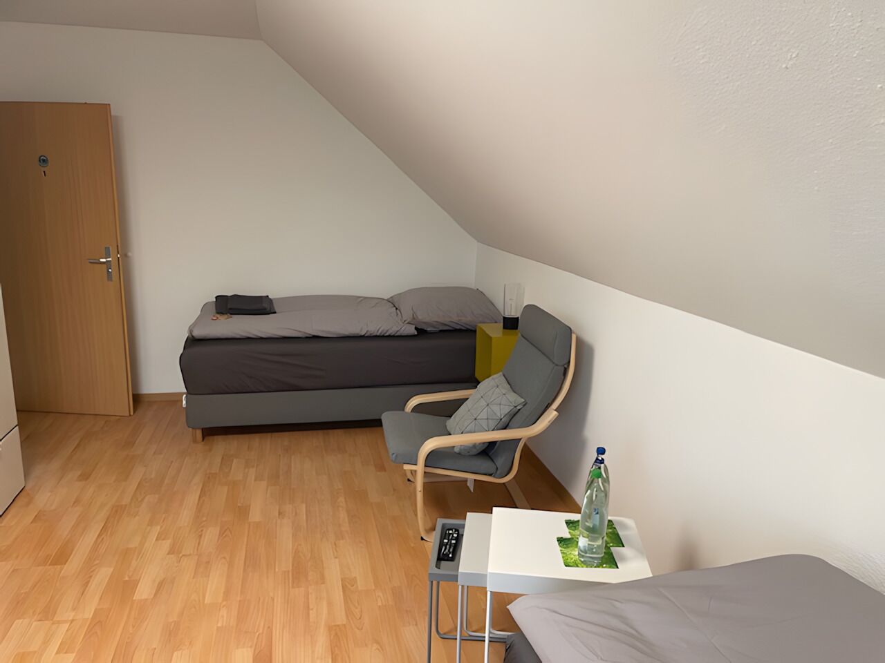 Et lille, moderne værelse med en seng, en stol, et lille bord og en dør.