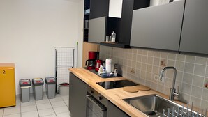 A modern kitchen with a wooden countertop, stainless steel sink, and grey cabinets. There are trash bins, a coffee maker, and a small plant on the counter.