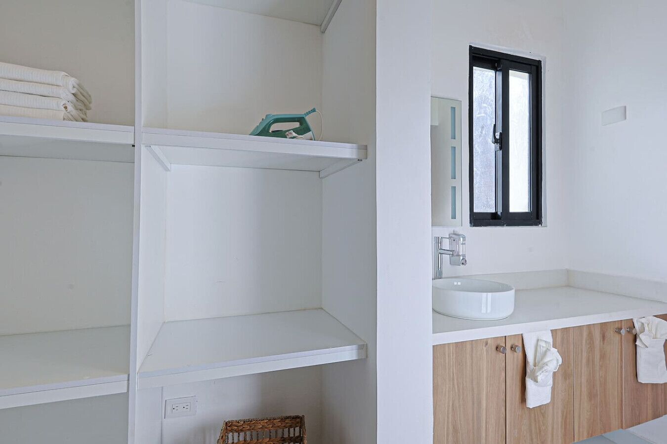 Un baño con estantes blancos, un lavamanos y un espejo.