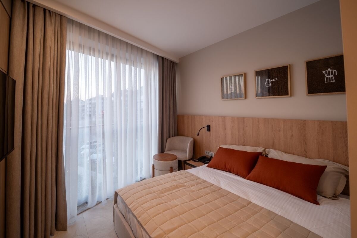 Une chambre d’hôtel avec un lit, une chaise, un bureau et une fenêtre avec des rideaux.