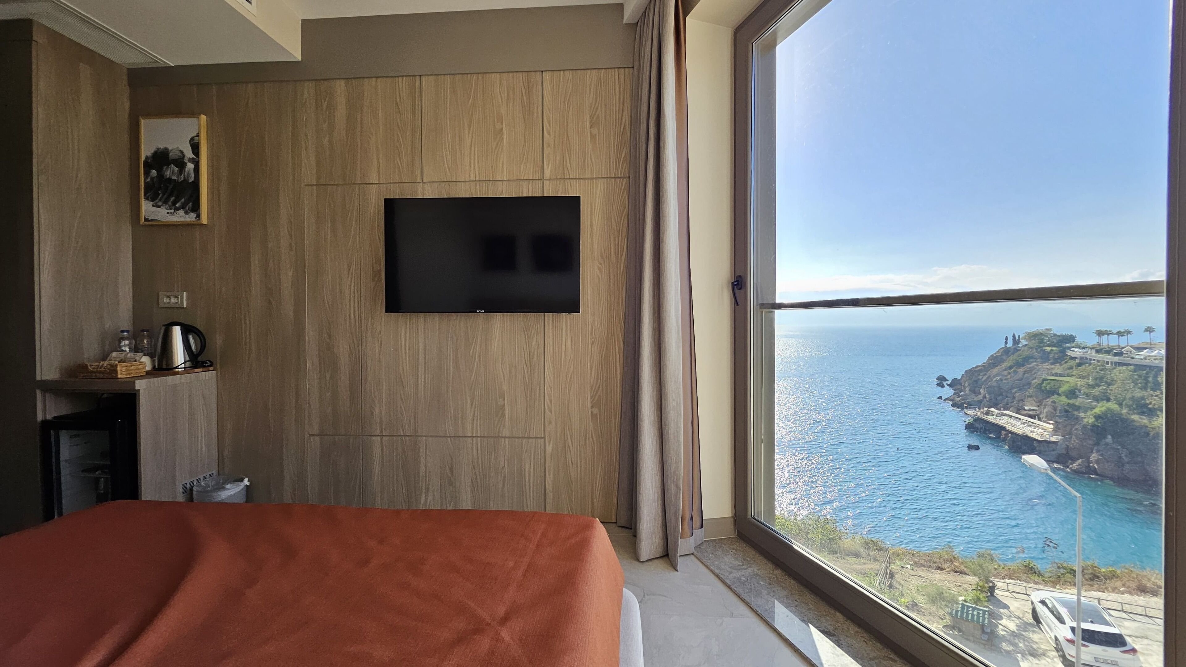 Une chambre d’hôtel avec un lit, un téléviseur fixé au mur, une fenêtre donnant sur la mer et un paysage côtier.