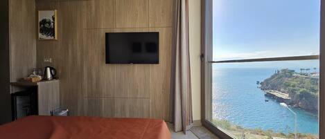 Une chambre d’hôtel avec un lit, un téléviseur fixé au mur, une fenêtre donnant sur la mer et un paysage côtier.