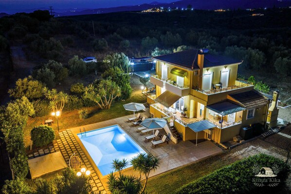 A two-story house with a swimming pool, outdoor seating, and a view of the surrounding landscape.