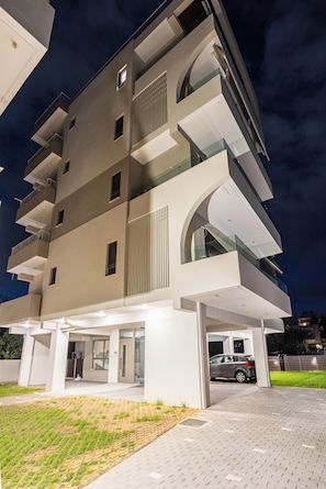 A modern multi-story building with a flat roof, large windows, and a covered entrance area.