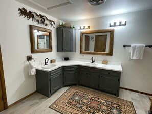 Uma casa de banho com lavatório de canto, duas espelhas, um porta-toalhas e um tapete estampado.