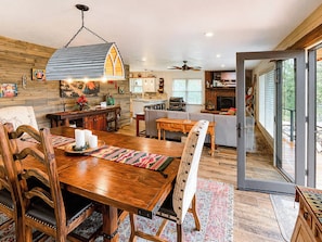 A spacious kitchen with a dining area, a fireplace, and a large sliding glass door leading to a balcony. - Luxury Mountain Cabin w/ Hot Tub & Fireplace (Ruidoso)