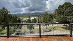 A wooden deck with a metal railing overlooking a landscape with trees and distant buildings. - Constancio's Cabin (Ruidoso)