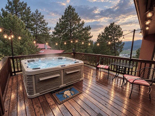 A hot tub on a wooden deck with string lights, surrounded by trees and a view of the landscape. - Luxury Mountain Cabin w/ Hot Tub & Fireplace (Ruidoso)
