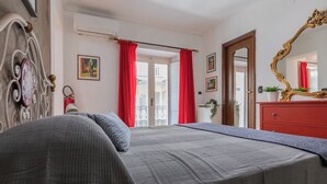 Une chambre à coucher avec un lit, une commode, un miroir et une fenêtre ornée de rideaux rouges.