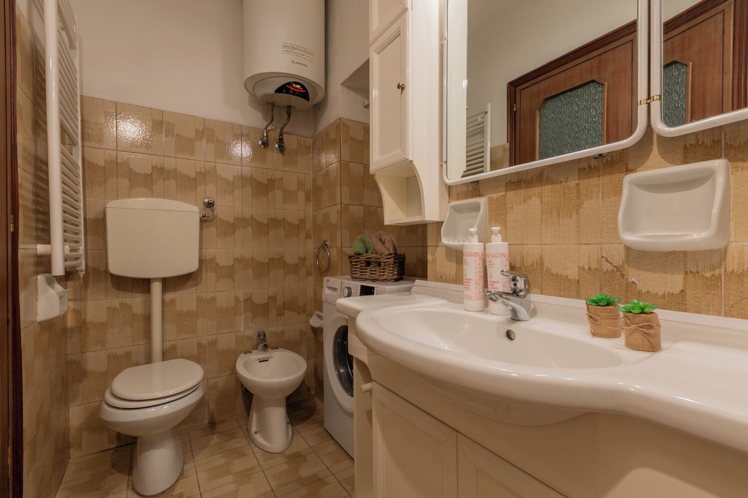 A bathroom with a toilet, bidet, washing machine, sink, and a mirror.