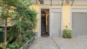 Une ruelle étroite, avec une petite entrée menant à un bâtiment dont la porte est fermée par un volet métallique.