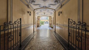 Un couloir orné de décorations complexes au plafond, doté d’un sol carrelé et de grilles en fer forgé noir.