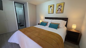 A hotel room with a bed, two pillows, a nightstand with a lamp, a wardrobe, and two wall-mounted artworks.