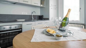 A modern kitchen with a dining table set for two, featuring a bottle of champagne, glasses, and a plate of chips. - La Croce Apartments (Castelnovo ne' Monti)